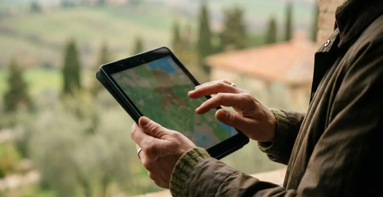 Fotografo che studia mappe digitali su tablet in campo aperto toscano